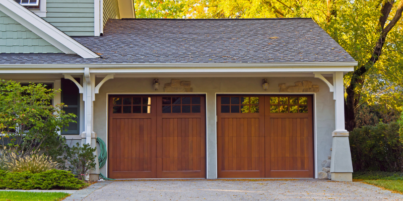 Front-facing attached garage with wooden paneled doors and pitched roof in a villa setting